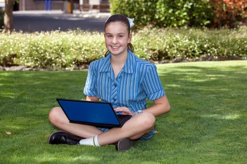 Smiling high school student working on laptop in the gardens