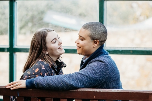 smiling lgbtqi couple looking at each other sitting on a bench - Australian Stock Image