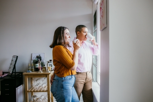 smiling lgbtqi couple drinking coffee looking outside the window