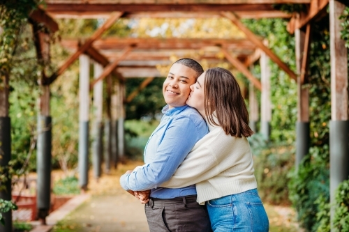 smiling lgbtqi couple hugging and kissing on the cheek