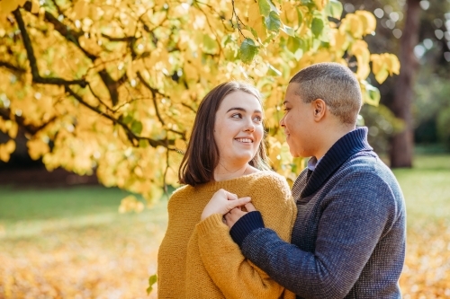 smiling lgbtqi couple looking at each other near autumn trees