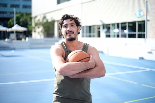 Smiling man holding basketball on blue court - Australian Stock Image