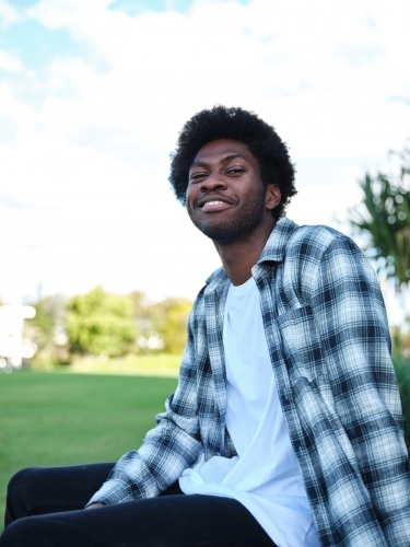Smiling man sitting on a concrete park bench wearing a checkered polo shirt