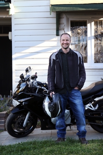 Smiling man standing in front of his motorbike - Australian Stock Image