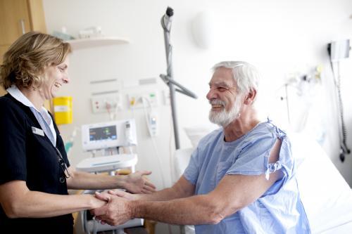 Smiling middle aged male patient shaking hands with a nurse in a hospital ward - Australian Stock Image