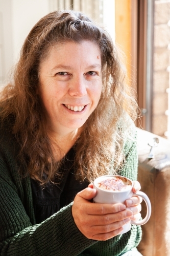 Smiling middle aged woman holding warm drink in mug - Australian Stock Image