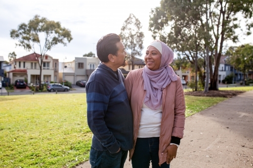 smiling middle aged woman wearing pink hijab and middle aged man looking at each other on a big lawn