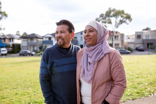 smiling middle aged woman wearing pink hijab and middle aged man wearing blue sweater looking away