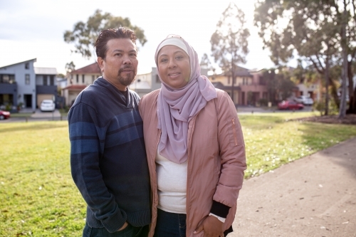 smiling middle aged woman wearing pink hijab and middle aged man wearing blue sweater looking away