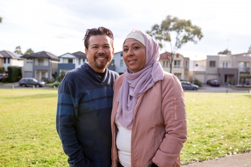 Smiling middle aged woman wearing pink hijab and smiling middle aged man wearing blue sweater