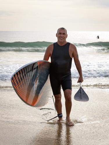 Smiling older man, holding surfboard and paddle - Australian Stock Image