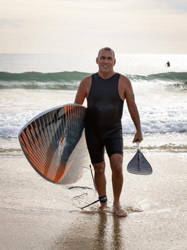 Smiling older man, holding surfboard and paddle