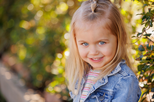 smiling preschool child sitting on edge of garden bed in bright sunny kindergarten yard - Australian Stock Image