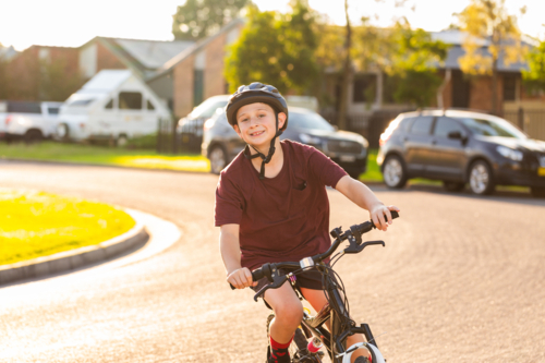 Smiling preteen boy riding along street in country town in golden sunlight - Australian Stock Image