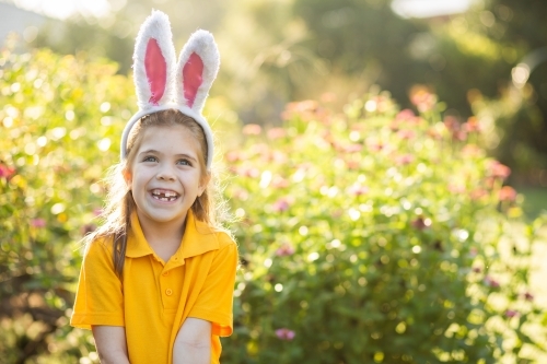 Smiling school kid outside in garden wearing rabbit ears for Easter celebrations - Australian Stock Image