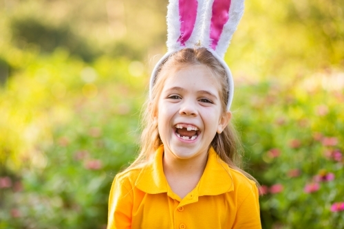 Smiling school kid outside in garden wearing rabbit ears for Easter celebrations - Australian Stock Image