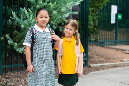 Smiling school kids outside public school with bags on - Australian Stock Image