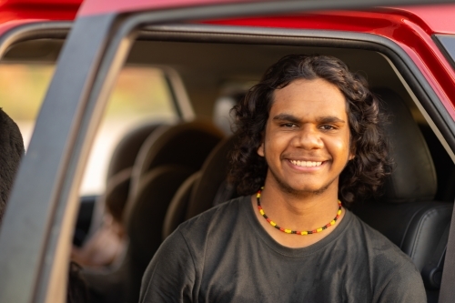 Smiling teenage boy from back seat with car door open - Australian Stock Image