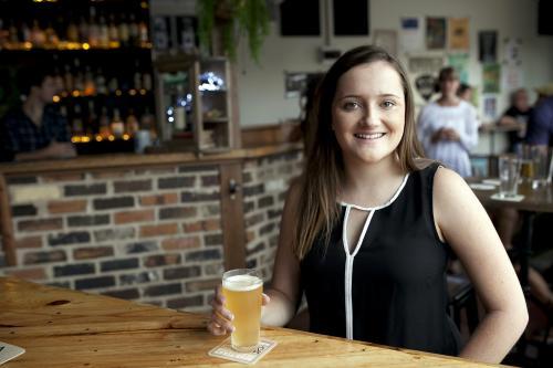 Smiling woman enjoying a drink at a local craft beer bar - Australian Stock Image