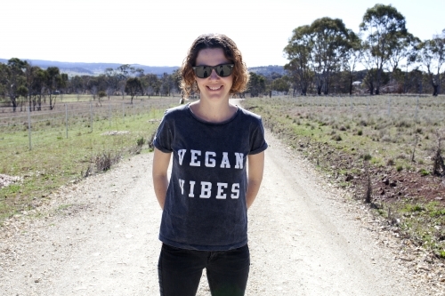 Smiling woman wearing vegan slogan t-shirt standing on rural dirt road - Australian Stock Image