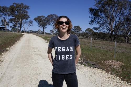 Smiling woman wearing vegan slogan t-shirt standing on rural dirt road - Australian Stock Image