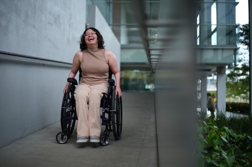 Smiling woman with a disability sitting in a wheelchair doing down the accessibility ramps - Australian Stock Image