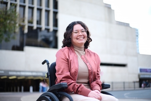 Smiling woman with a disability sitting in a wheelchair outside - Australian Stock Image