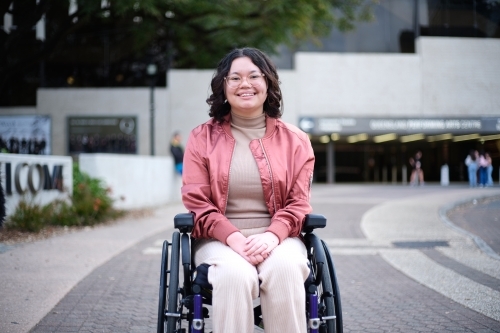 Smiling woman with a disability sitting in a wheelchair outside - Australian Stock Image
