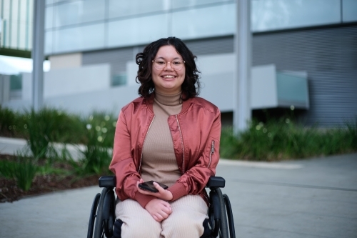 Smiling woman with a disability sitting in a wheelchair outside - Australian Stock Image
