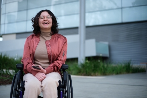 Smiling woman with a disability sitting in a wheelchair outside - Australian Stock Image
