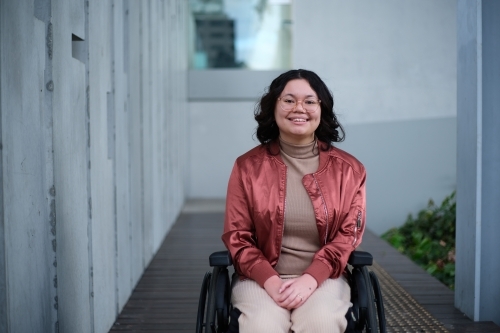 Smiling woman with a disability sitting in a wheelchair outside - Australian Stock Image
