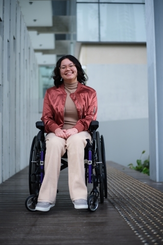 Smiling woman with a disability sitting in a wheelchair outside - Australian Stock Image