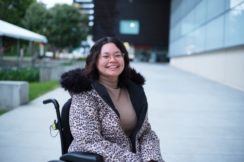 Smiling woman with a disability sitting in a wheelchair outside - Australian Stock Image