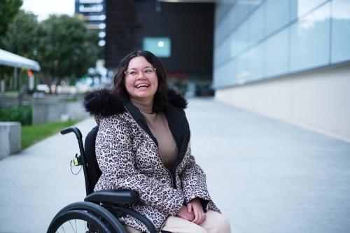 Smiling woman with a disability sitting in a wheelchair outside - Australian Stock Image