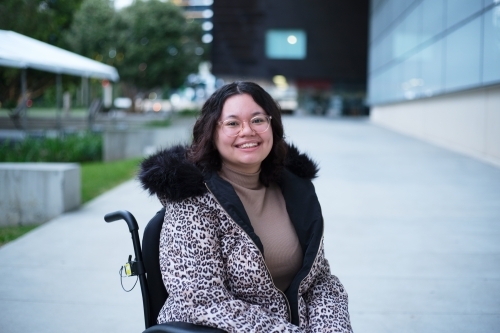 Smiling woman with a disability sitting in a wheelchair outside - Australian Stock Image