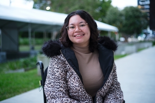 Smiling woman with a disability sitting in a wheelchair outside - Australian Stock Image