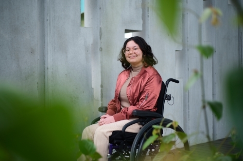 Smiling woman with a disability sitting in a wheelchair outside in urban setting with greenery