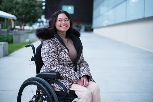Smiling woman with a disability sitting in a wheelchair outside on cold day - Australian Stock Image