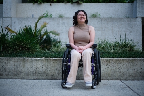 Smiling woman with a disability sitting in a wheelchair outside with grass and plants behind her
