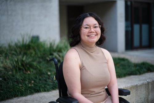 Smiling woman with a disability sitting in a wheelchair outside with grass and plants behind her - Australian Stock Image