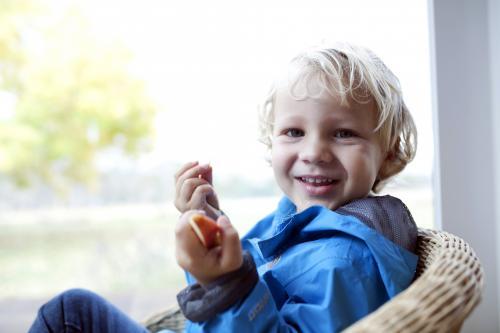 Smiling young boy wearing a blue jacket eating pieces of apple