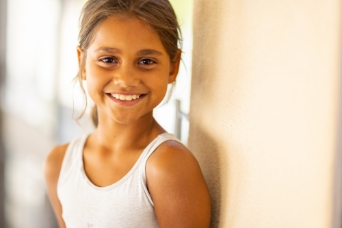smiling young girl in white singlet leaning on the wall - Australian Stock Image