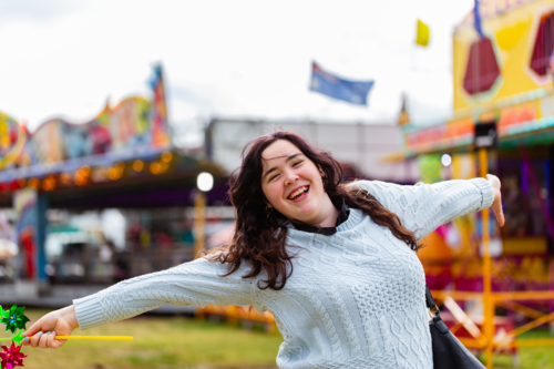 Smiling young woman at country show event smiling and holding a pinwheel on windy day - Australian Stock Image