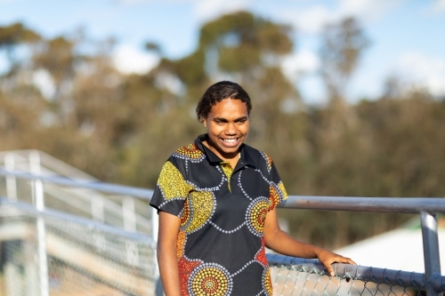 smiling young woman holding handrail with trees in background - Australian Stock Image
