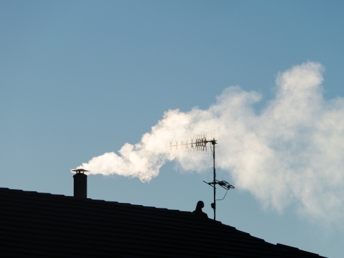 Smoke billowing from a chimney through a TV aerial against a blue sky