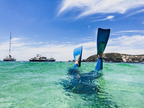 Snorkellers fins kicking above clear ocean  water with boats and coast in background - Australian Stock Image