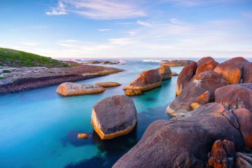 Soft evening light washes over the granite boulders and turquoise waters of Elephant Rocks - Australian Stock Image