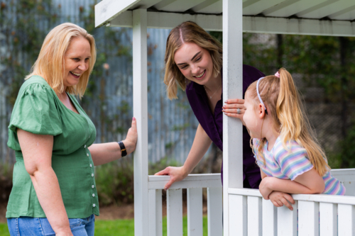 Speech therapist professional with girl interacting by cubby house talking and assessing child - Australian Stock Image
