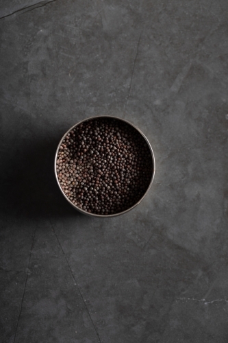 Spice tin of black mustard seeds on a dark marble background