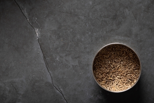 Spice tin of cumin seeds on dark marble background - Australian Stock Image